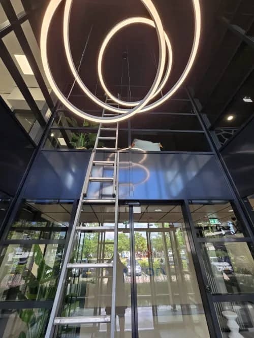 Glazenwasser met ladder in een kantoorentree met hoge glazen pui en ronde hanglampen