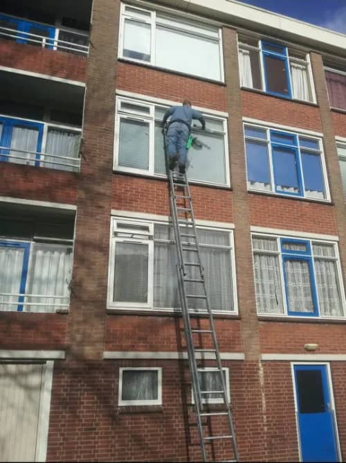 Glazenwasser van De Blinkende Jager wast op een ladder de ramen van een appartementencomplex