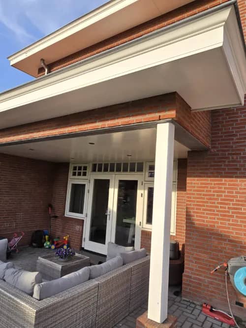 Overkapt terras van een woning met tuinmeubels en een schoongemaakte pui
